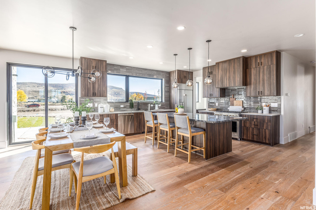 Kitchen featuring light hardwood / wood-style floors, a center island, backsplash, an inviting chandelier, and pendant lighting