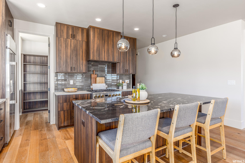Kitchen with a kitchen bar, a kitchen island, light hardwood / wood-style floors, backsplash, and decorative light fixtures