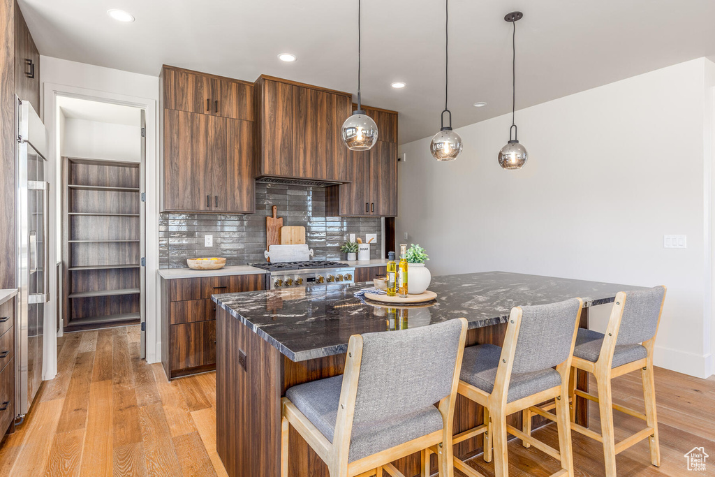 Kitchen featuring decorative backsplash, a breakfast bar, stainless steel stove, light wood-type flooring, and a center island