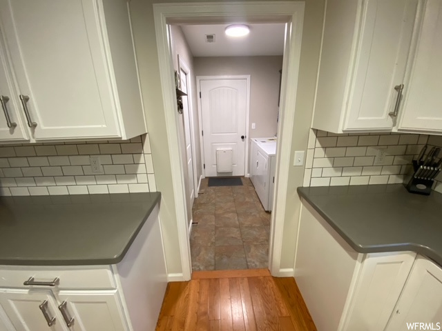 Kitchen featuring light hardwood / wood-style floors, washing machine and clothes dryer, white cabinets, and tasteful backsplash