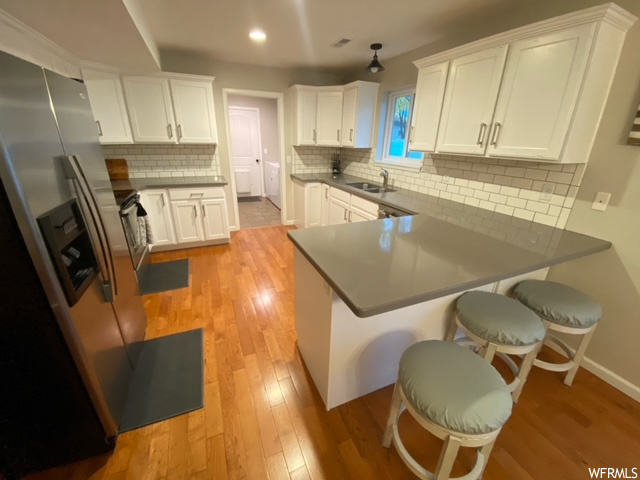Kitchen with stainless steel refrigerator, a breakfast bar area, light wood-type flooring, white cabinets, and kitchen peninsula