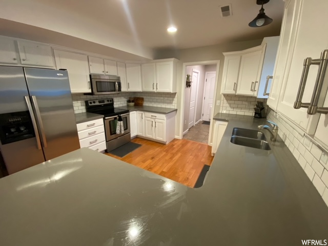 Kitchen featuring sink, light hardwood / wood-style floors, backsplash, white cabinetry, and stainless steel appliances