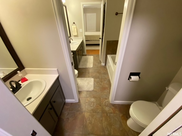 Bathroom with double vanity, tile floors, a washtub, and toilet