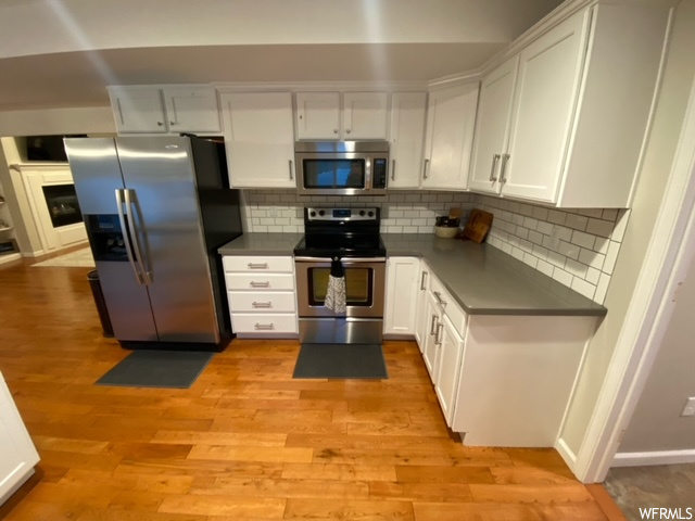 Kitchen featuring light hardwood / wood-style floors, tasteful backsplash, stainless steel appliances, white cabinets, and a fireplace