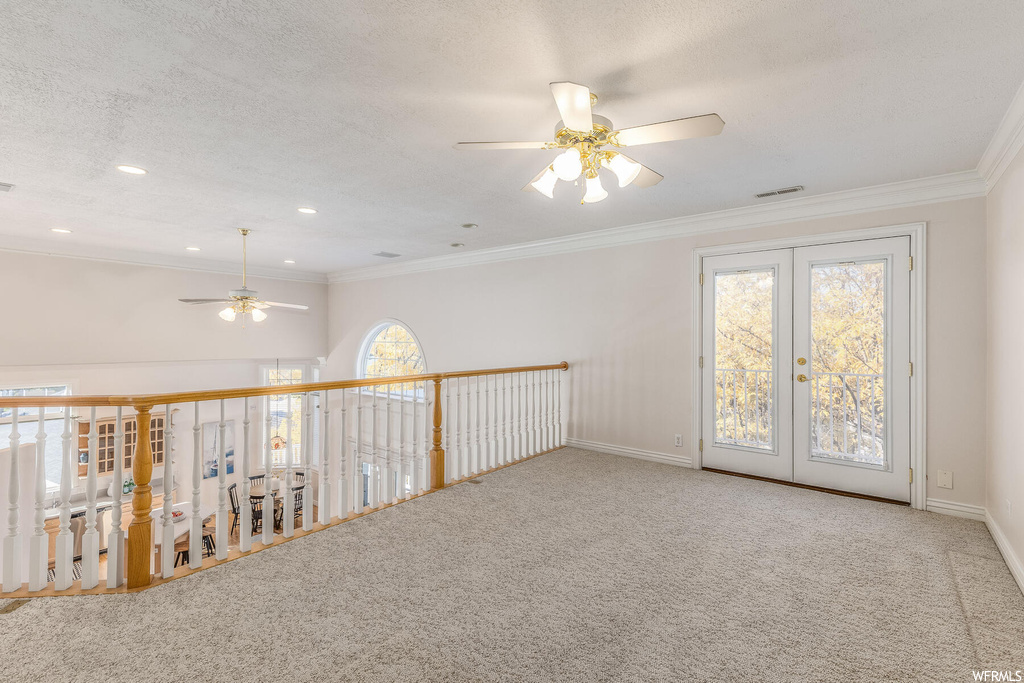 Unfurnished room featuring light carpet, ornamental molding, ceiling fan, and a healthy amount of sunlight