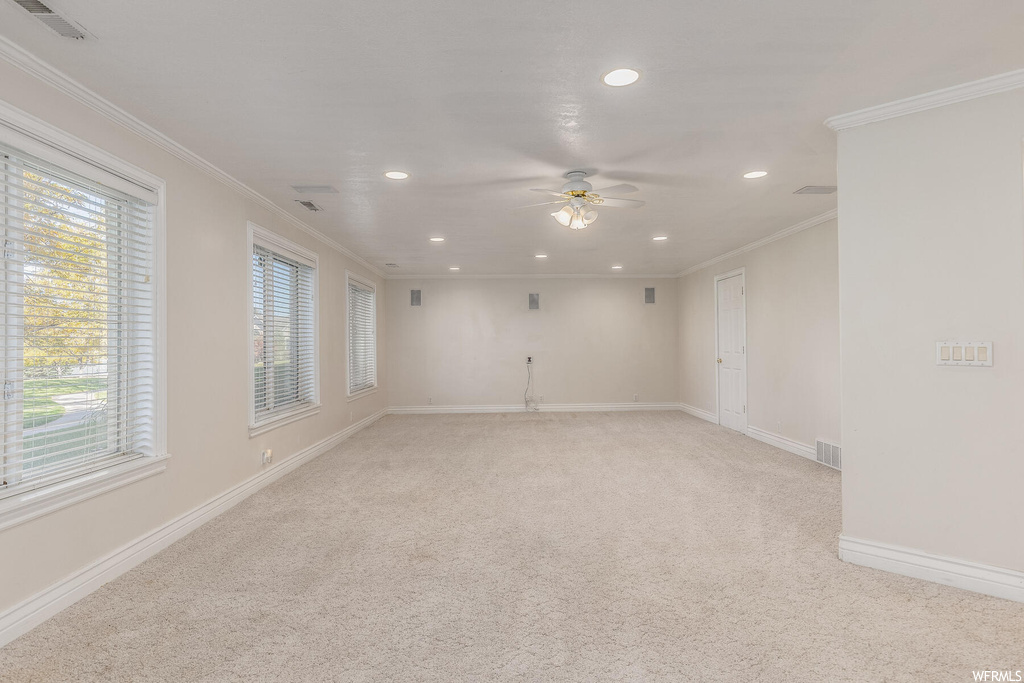 Empty room featuring ceiling fan, crown molding, and light colored carpet