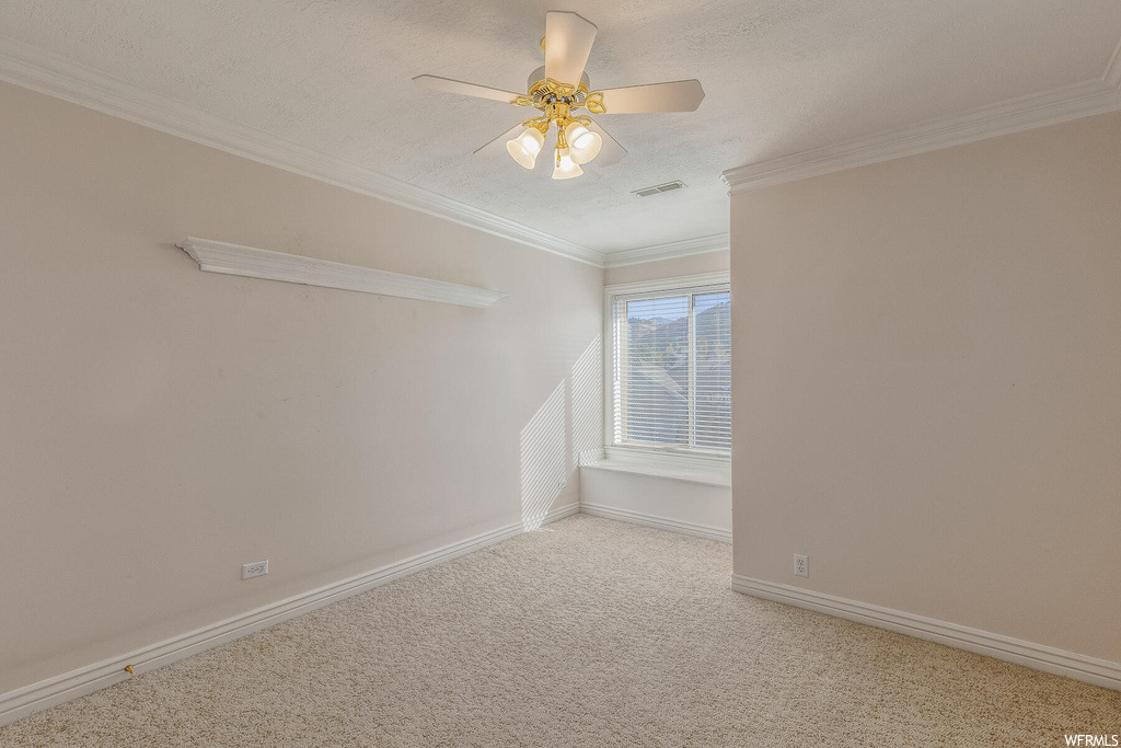 Spare room featuring light colored carpet, ceiling fan, and ornamental molding