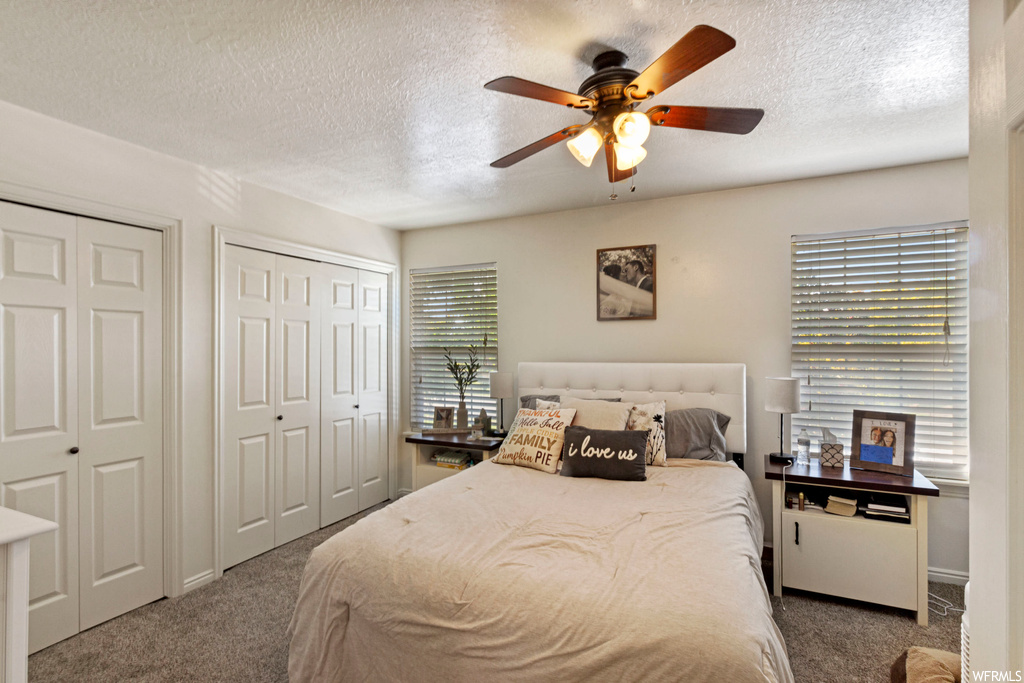 Bedroom featuring multiple closets, multiple windows, ceiling fan, and dark carpet