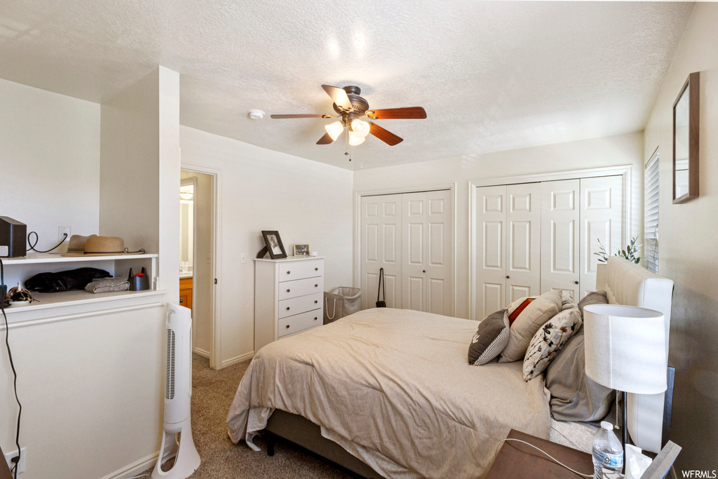 Carpeted bedroom featuring ceiling fan, multiple closets, and a textured ceiling