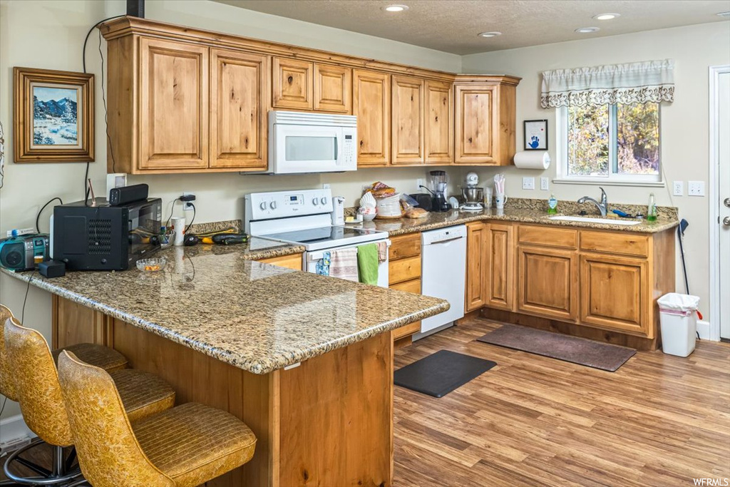 Kitchen featuring a kitchen bar, sink, light wood-type flooring, light stone counters, and white appliances