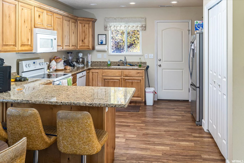 Kitchen featuring sink, white appliances, dark hardwood / wood-style flooring, a kitchen breakfast bar, and light stone counters