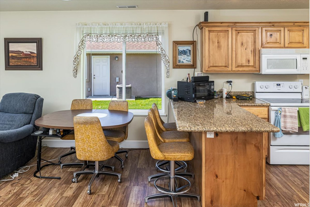 Kitchen with a kitchen bar, dark wood-type flooring, a kitchen island, white appliances, and light stone counters