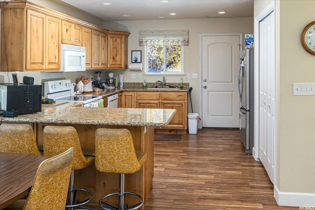 Kitchen with a breakfast bar area, dark hardwood / wood-style floors, sink, light stone countertops, and white appliances