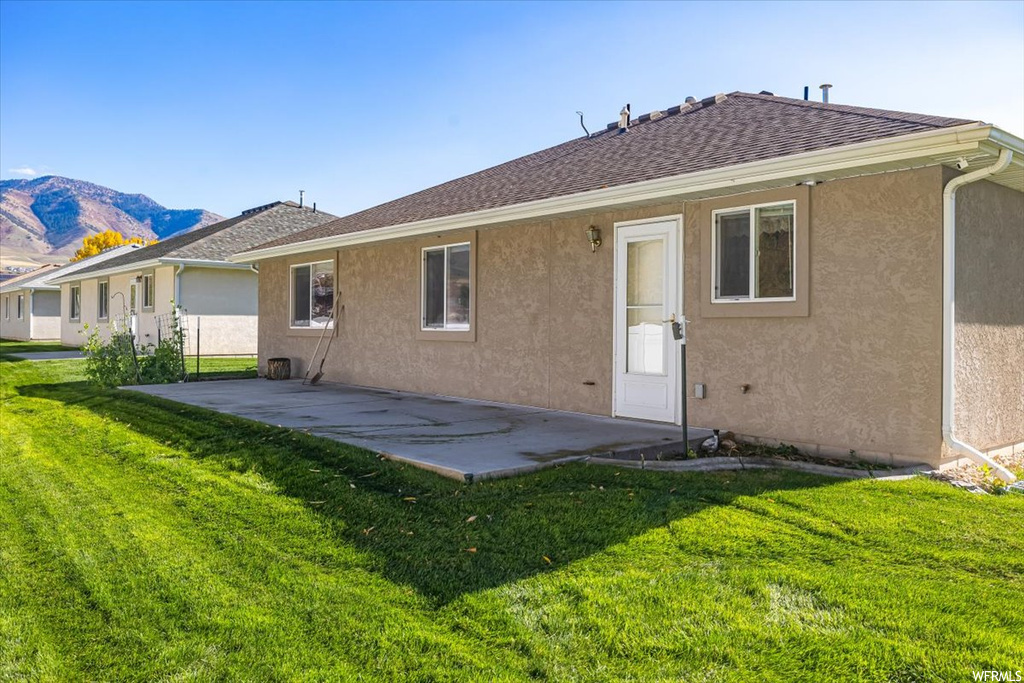 Back of property featuring a patio area, a mountain view, and a lawn