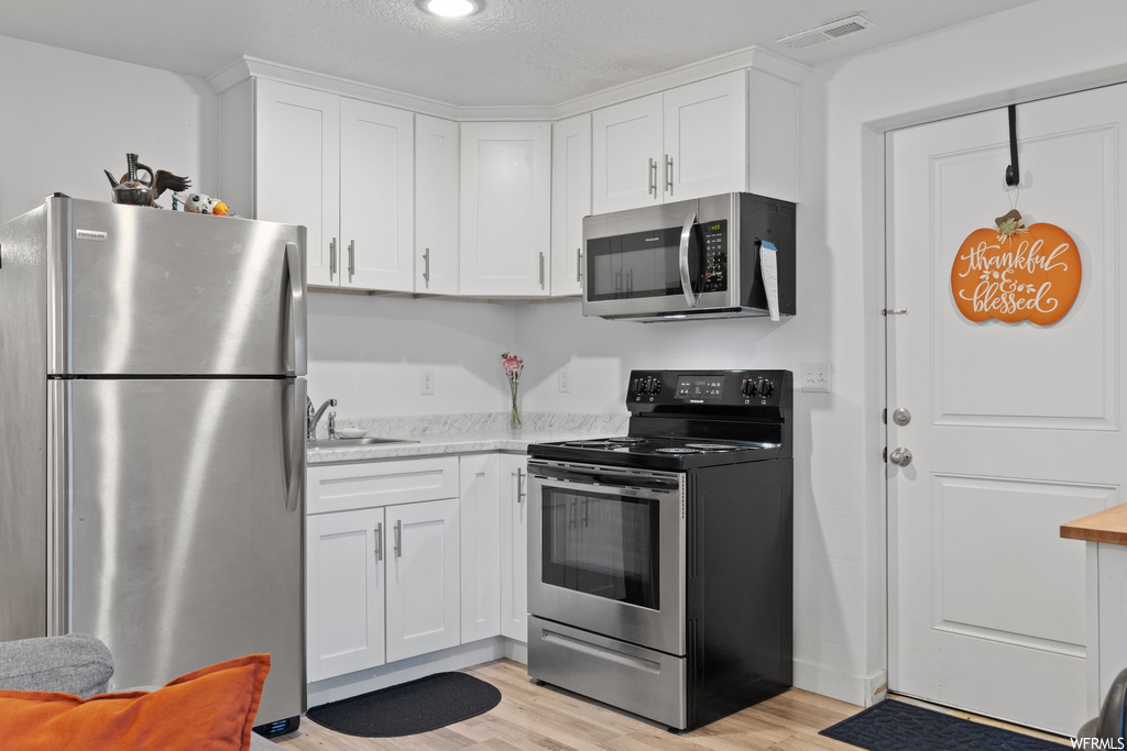 Kitchen featuring stainless steel appliances, light hardwood / wood-style floors, white cabinets, and sink