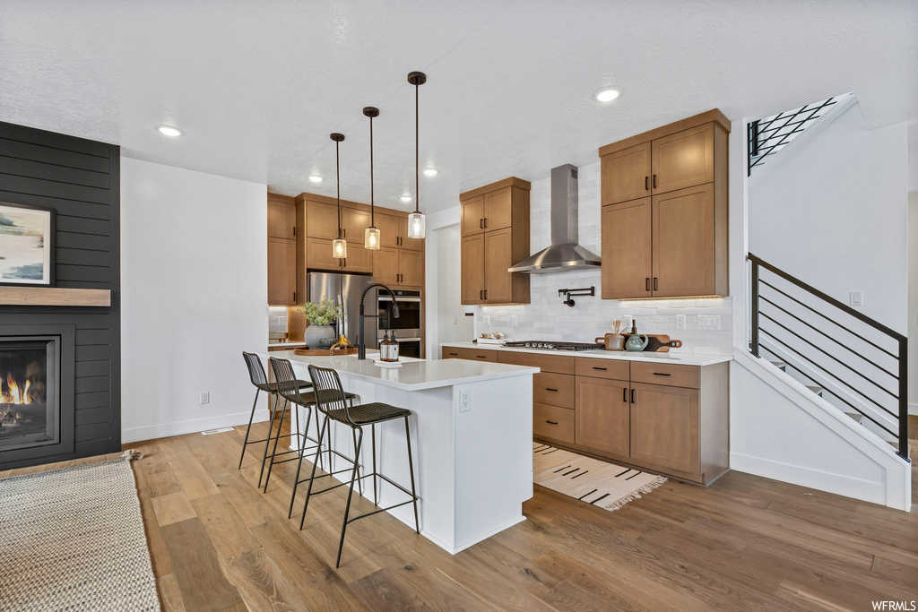 Kitchen with hanging light fixtures, a fireplace, light hardwood / wood-style floors, backsplash, and wall chimney range hood