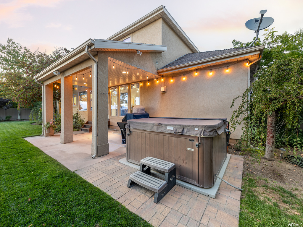 Patio terrace at dusk with a hot tub and a lawn