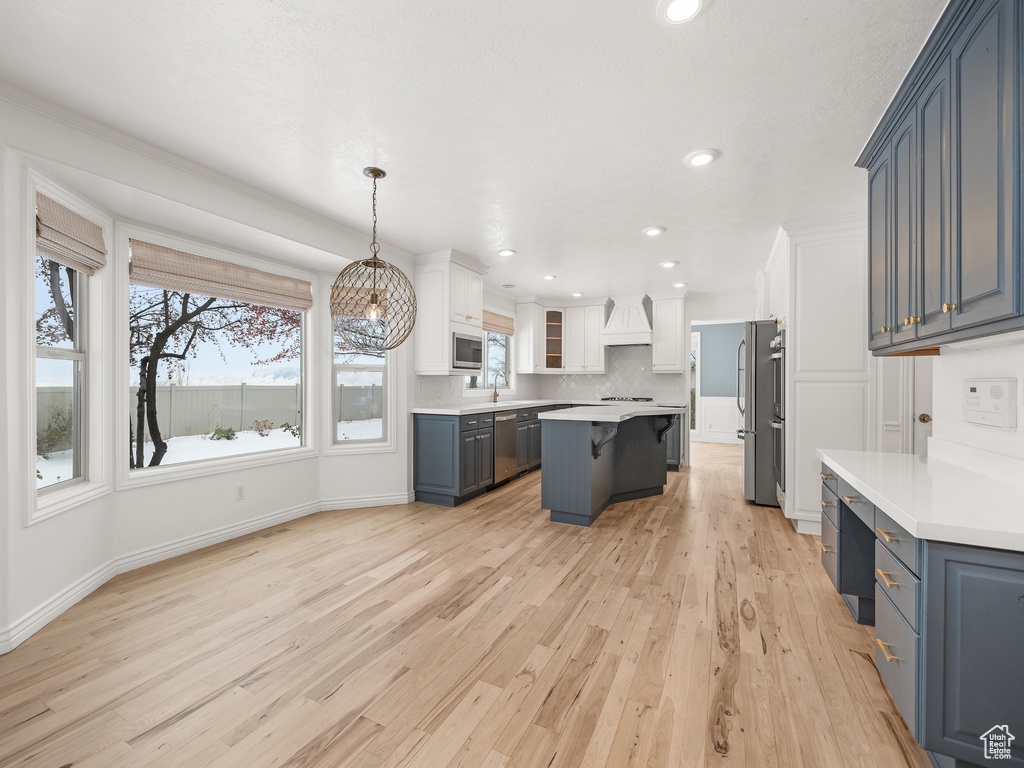 Kitchen with a kitchen island, pendant lighting, light hardwood / wood-style flooring, and a healthy amount of sunlight