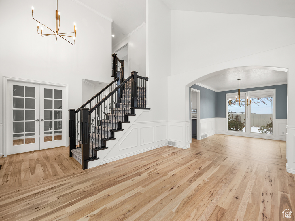 Entrance foyer with light hardwood / wood-style floors, french doors, a notable chandelier, high vaulted ceiling, and ornamental molding