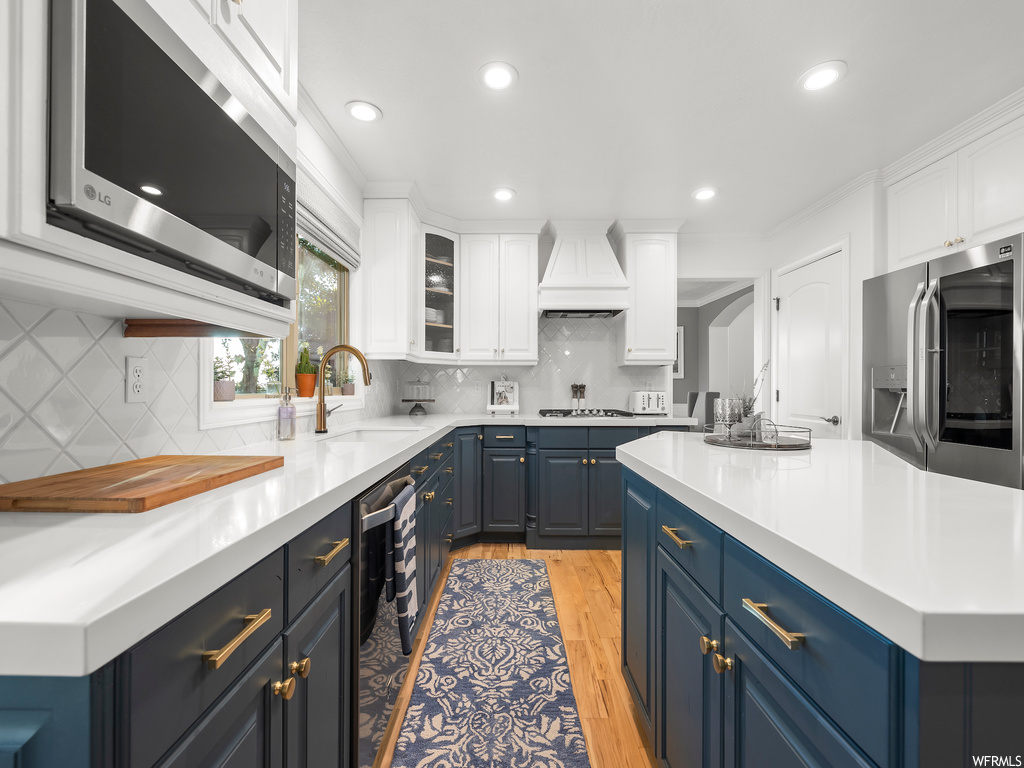 Kitchen with tasteful backsplash, sink, light wood-type flooring, white cabinets, and custom range hood