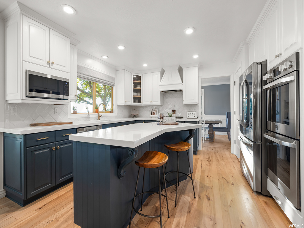 Kitchen featuring a kitchen island, premium range hood, light hardwood / wood-style flooring, and white cabinetry
