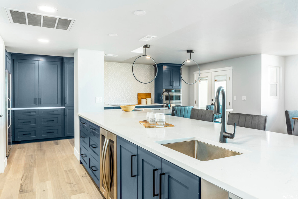 Kitchen featuring sink, light hardwood / wood-style flooring, stainless steel oven, hanging light fixtures, and blue cabinetry