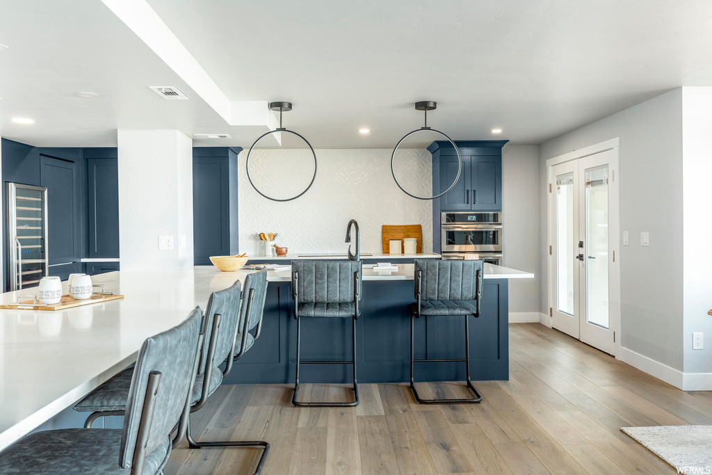 Kitchen featuring blue cabinets, double oven, decorative light fixtures, light hardwood / wood-style flooring, and a kitchen breakfast bar