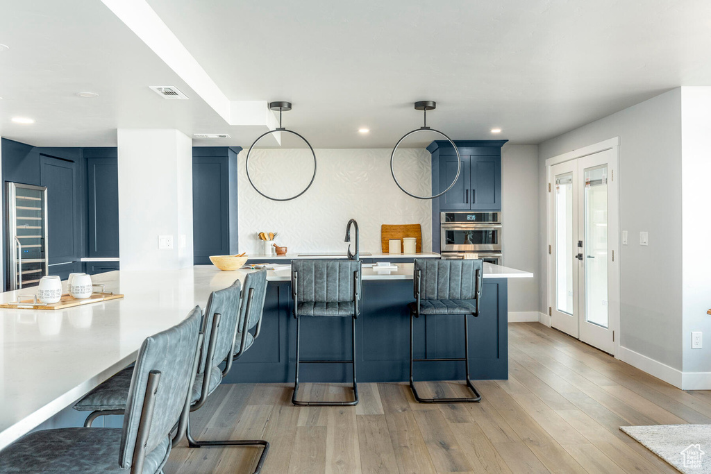 Kitchen featuring a breakfast bar, french doors, blue cabinets, hanging light fixtures, and light hardwood / wood-style flooring