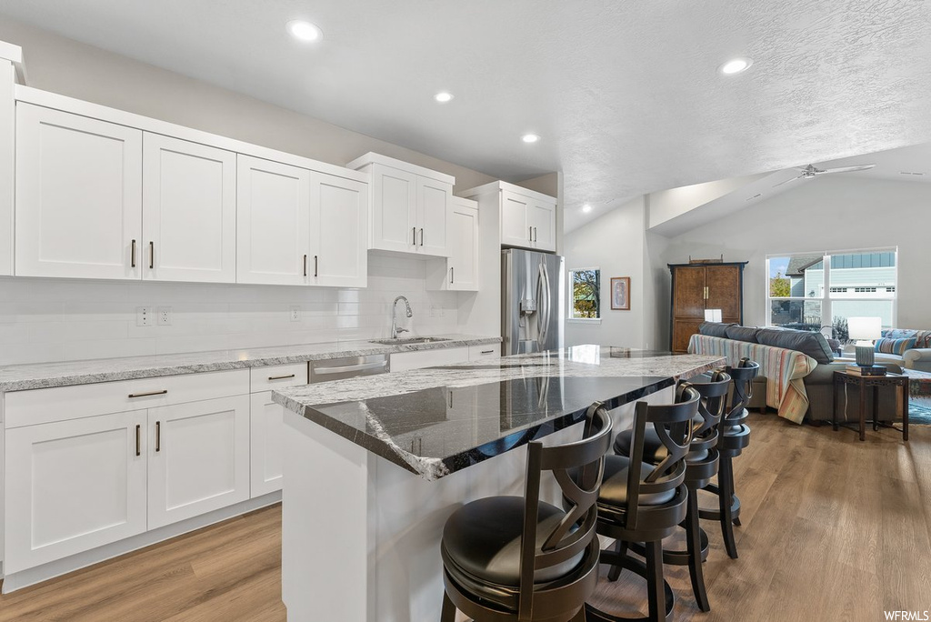 Kitchen with a breakfast bar area, light hardwood / wood-style floors, light stone countertops, white cabinets, and vaulted ceiling