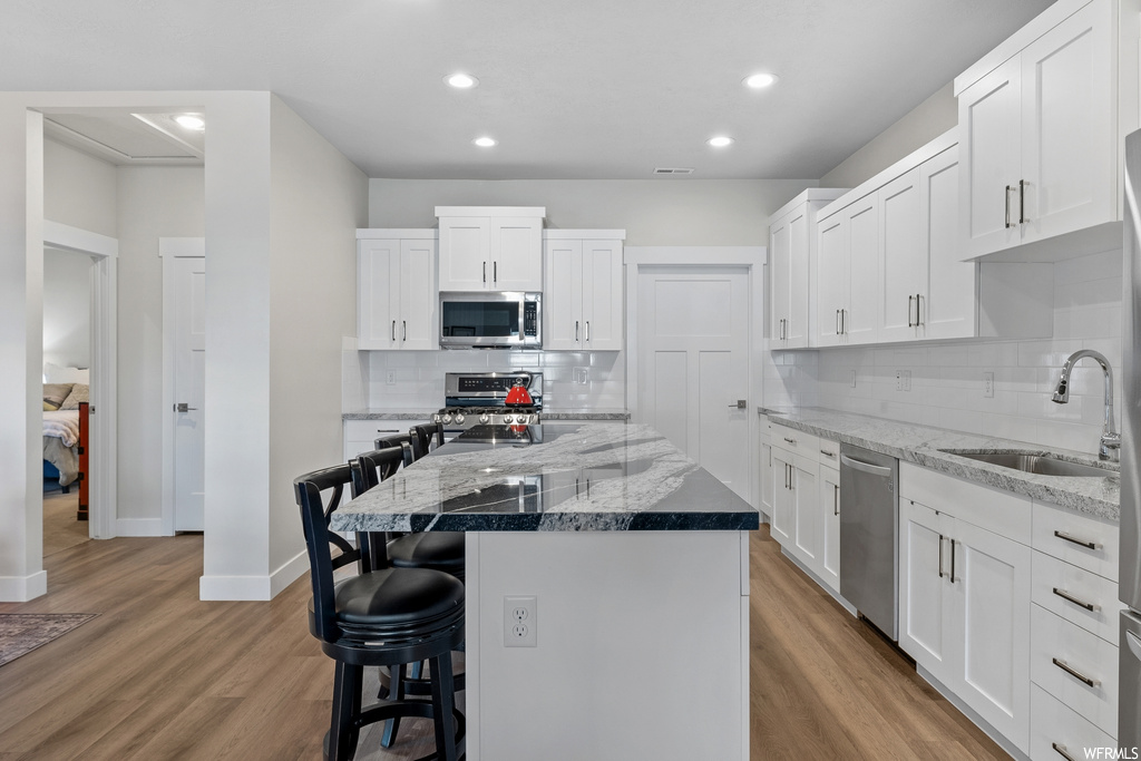 Kitchen featuring stainless steel appliances, a kitchen island, light wood-type flooring, and tasteful backsplash