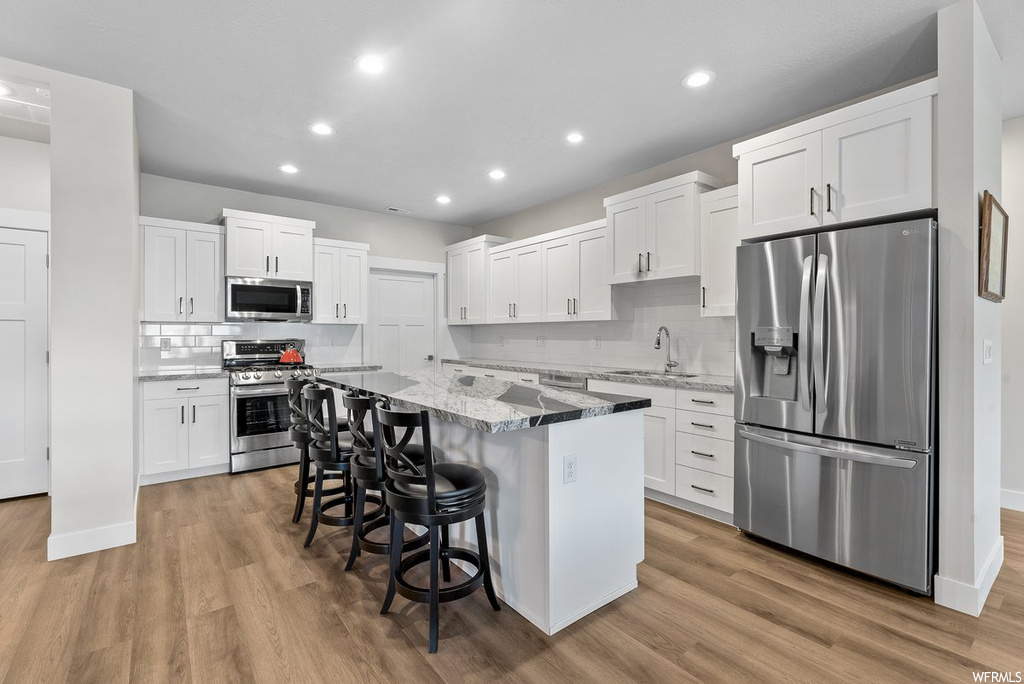 Kitchen featuring tasteful backsplash, light hardwood / wood-style flooring, a center island, white cabinets, and stainless steel appliances