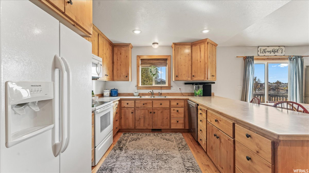 Kitchen featuring plenty of natural light, light wood-type flooring, kitchen peninsula, and white appliances