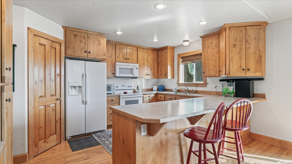 Kitchen with sink, light wood-type flooring, kitchen peninsula, white appliances, and a kitchen breakfast bar