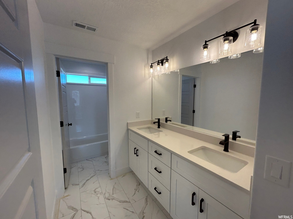Bathroom with dual vanity, a textured ceiling, tile flooring, and shower / bathtub combination
