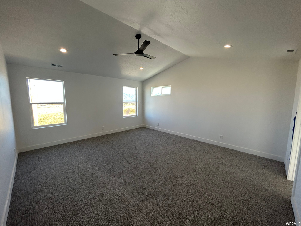 Carpeted spare room featuring plenty of natural light, ceiling fan, and vaulted ceiling