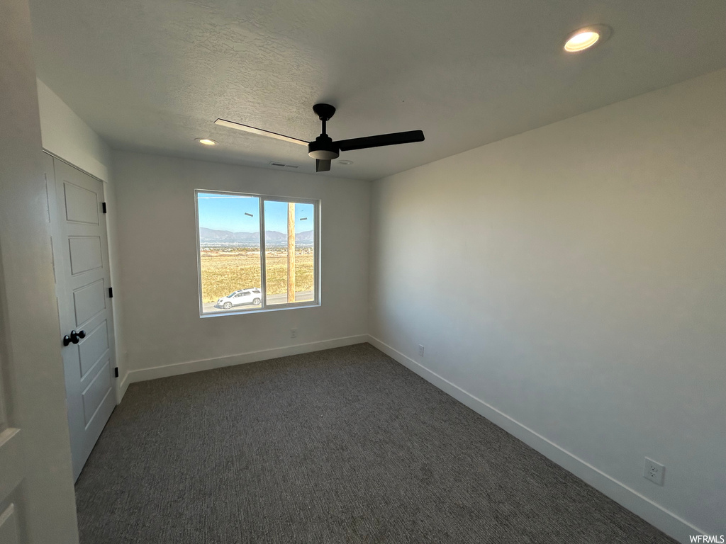 Empty room featuring a textured ceiling, ceiling fan, and dark colored carpet