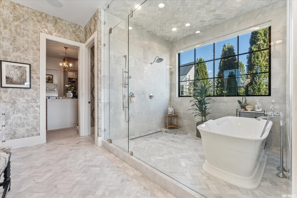Bathroom with tile walls, shower with separate bathtub, tile flooring, and an inviting chandelier