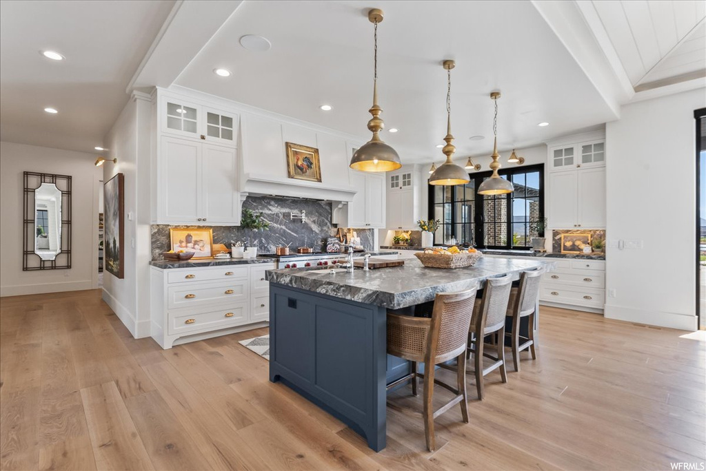 Kitchen with light hardwood / wood-style floors, an island with sink, a kitchen breakfast bar, white cabinets, and pendant lighting