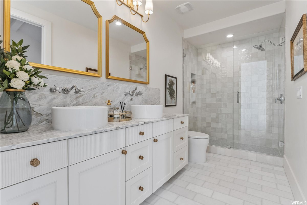 Bathroom featuring an enclosed shower, toilet, tile walls, double sink vanity, and tile floors