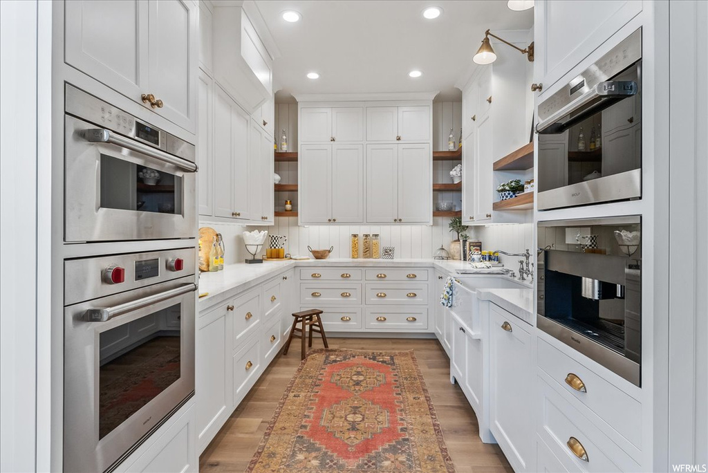Kitchen featuring stainless steel double oven, white cabinets, tasteful backsplash, and light hardwood / wood-style flooring