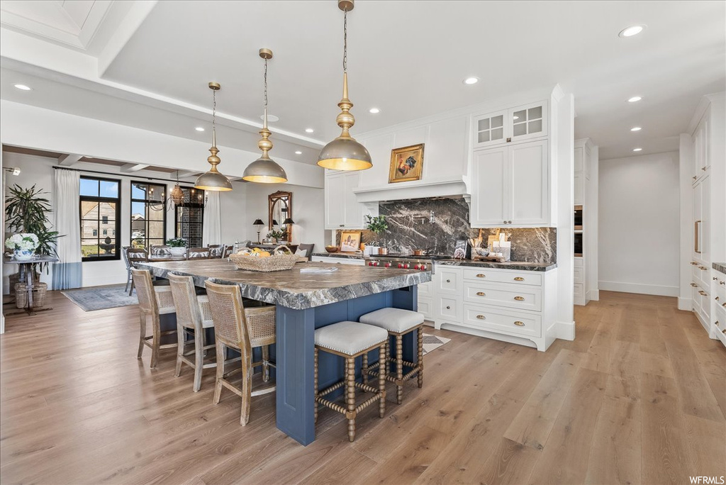 Kitchen with a kitchen island with sink, backsplash, white cabinets, and light hardwood / wood-style floors