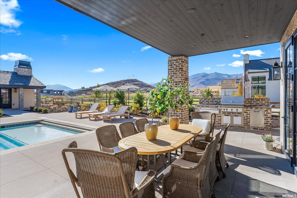 View of patio featuring a mountain view, an outdoor kitchen, a grill, and a fenced in pool
