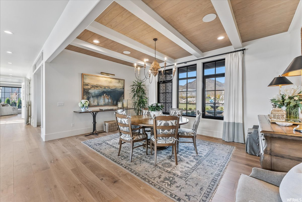 Dining area with light hardwood / wood-style floors, beam ceiling, and a notable chandelier