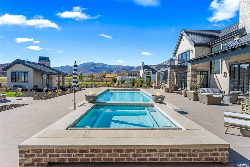 View of swimming pool featuring a patio area, a mountain view, and an in ground hot tub