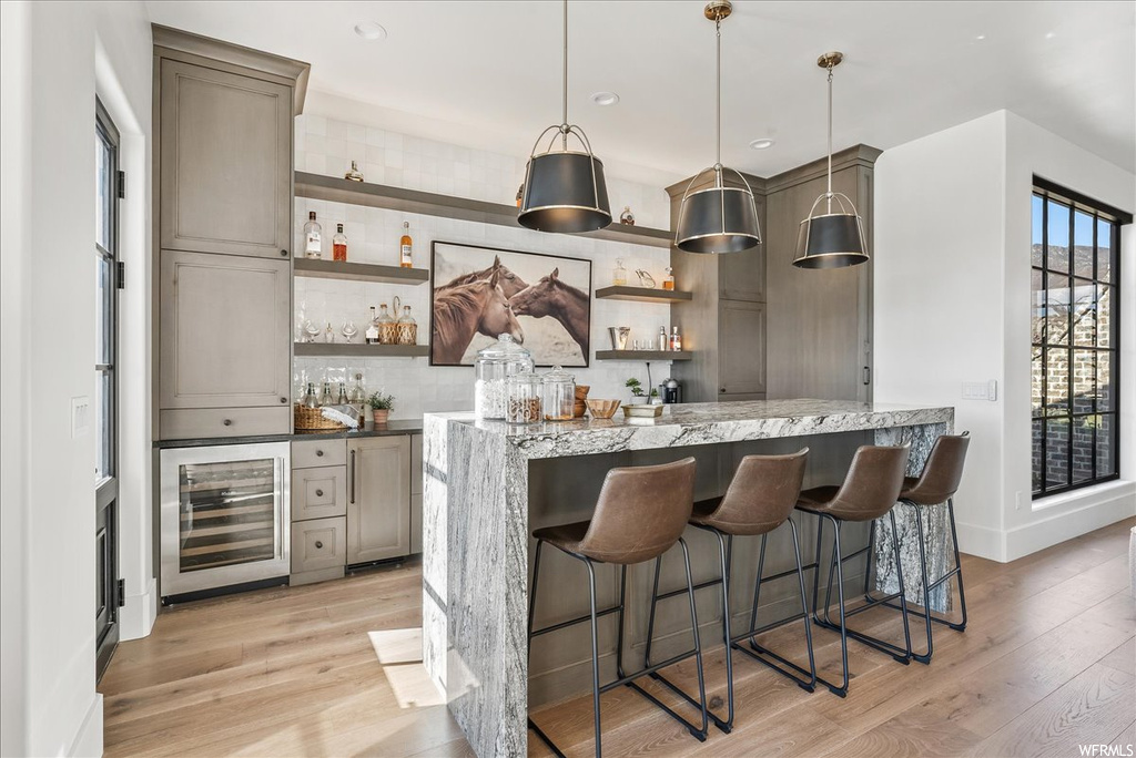 Kitchen with light hardwood / wood-style floors, decorative light fixtures, gray cabinets, wine cooler, and tasteful backsplash