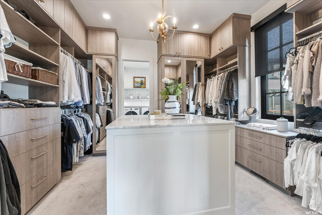 Walk in closet featuring light colored carpet, washer and clothes dryer, and a notable chandelier