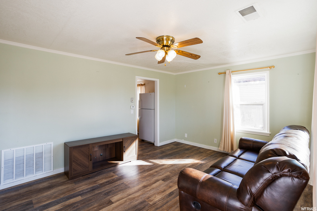 Living room with crown molding, ceiling fan, and dark wood-type flooring