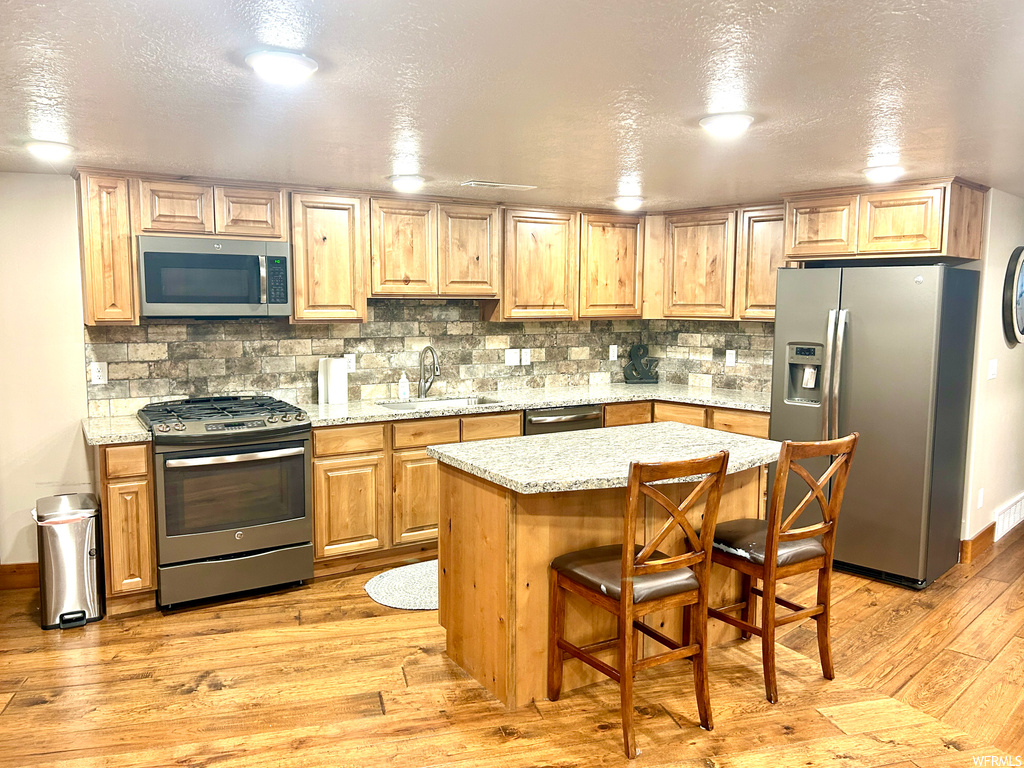 Kitchen featuring tasteful backsplash, sink, light wood-type flooring, stainless steel appliances, and a kitchen breakfast bar