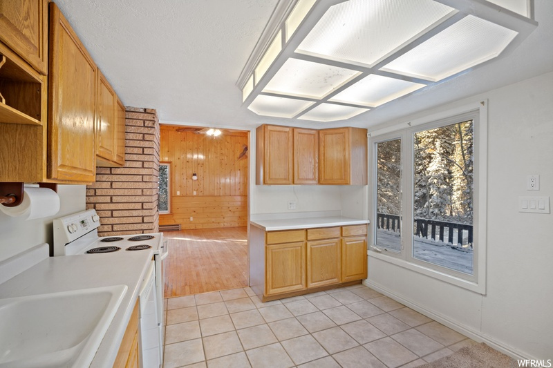 Kitchen with wood walls, white electric range, light tile floors, and sink