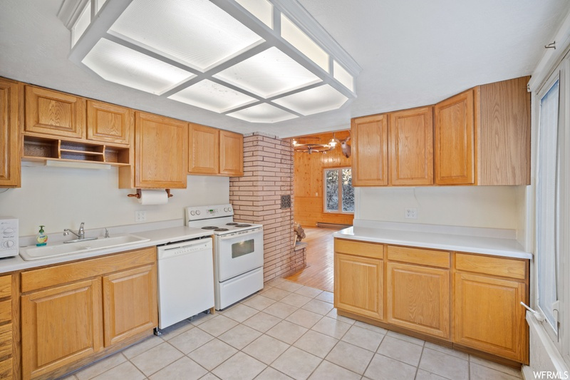 Kitchen with white appliances, sink, light tile floors, and brick wall